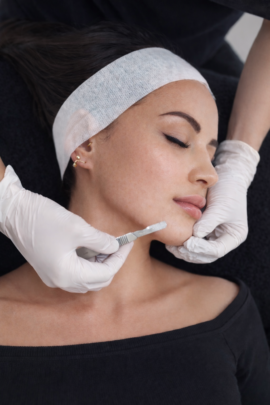 Woman receiving a facial treatment with gloved hands performing a dermaplaning treatment.